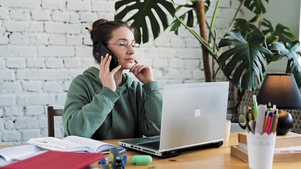 White Woman in Glasses Working From Home and Talking on the Phone While Typing on Computer