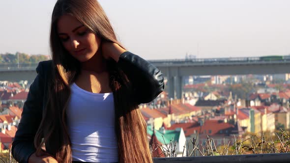 Young Beautiful Woman Looks Around - City with Buildings in the Background