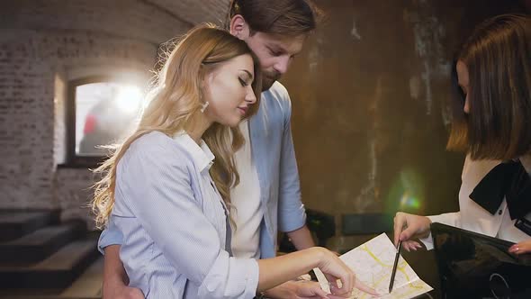 Man Hugging His Blond Smiling Girlfriend while Listening about Interesting Places Around Hotel