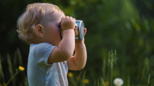 one year old baby spills liquid from a metal mug. The concept of walking outdoors,