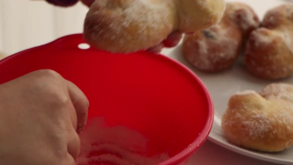 Hands putting sugar from a red bowl on delicious fresh Christmas buns