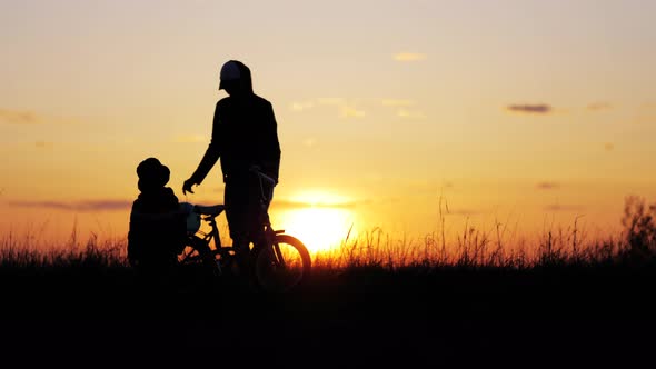 Silhouette of Mother Teaching Little Son to Ride a Bike at Meadow During Sunset