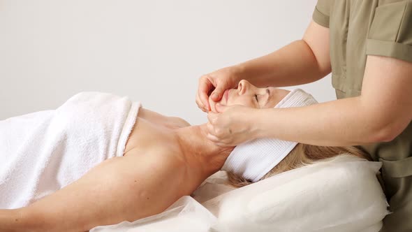 Beauty Salon Therapist in Coat Massages Lying Woman Cheeks