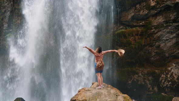 Young Woman Traveler Admires the Scale of the Waterfall While Standing on the Edge