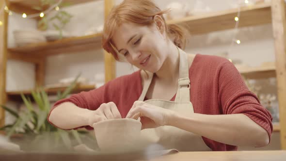 Young Woman Sculpting Earthenware Vessel in Pottery Workshop