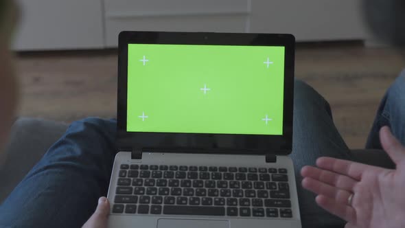 Man and Woman at Home Using Green Mock-up Screen Laptop Computer While Sitting on Couch in Living