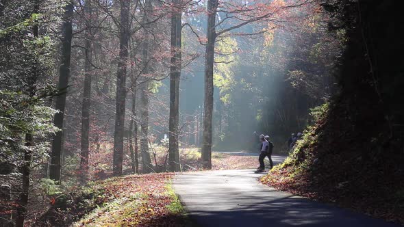 A group of young men ride their longboard skateboards downhill on a forest road in the fog.