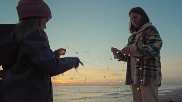 Mother With Her Daughter On The Beach With Lights