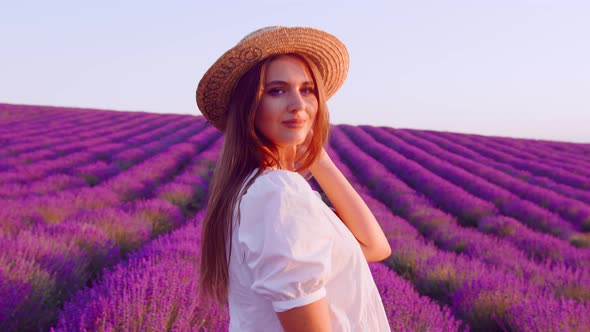 Beautiful Young Woman Wearing White Dress and Hat Standing in a Lavender Field