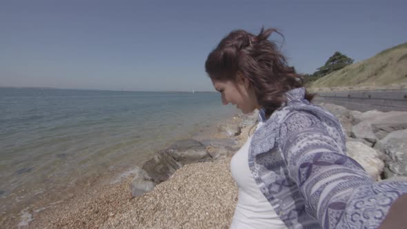 POV Shot Of Young Woman Reaching Down To Pick Up Plastic Bottle On Beach - Ungraded