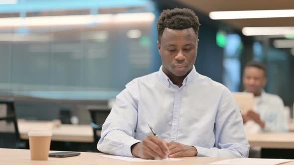 Pensive African Businessman Writing on Paper Thinking