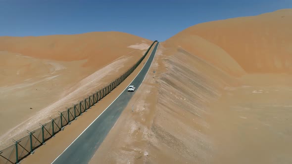 Aerial view of white car driving uphill in road in the desert, Abu Dhabi, UAE.