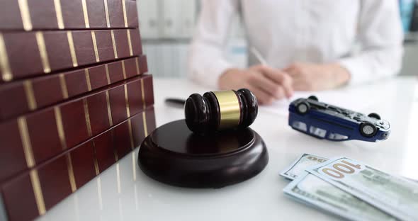 Judge Gavel with Money and Overturned Toy Car Lying Against Background of Woman with Documents