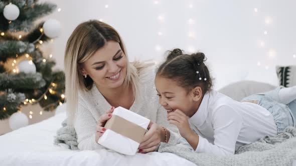 Mother and Daughter with Gift Laying on Bed Near Christmas Tree