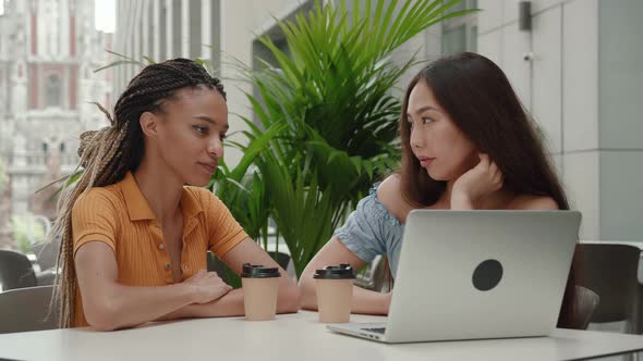 Two Young Mixed Race Girls Have Cute Conversation While Sitting Outdoors in a Summer Cafe of the