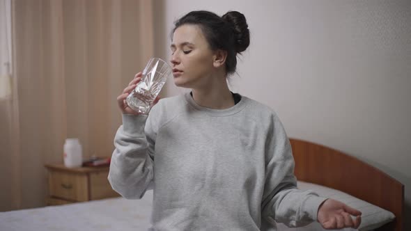 Portrait of Confident Young Woman Taking Pill Washing Off Medication with Water Smiling Looking at