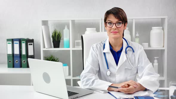 Portrait Smiling Mature Female Doctor in Uniform Wearing Glasses Posing at Modern Workplace