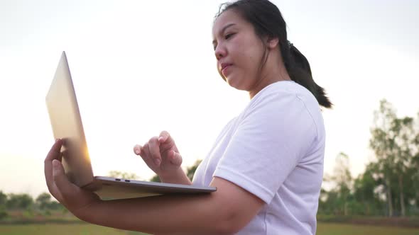 Asian woman woking on laptop in field