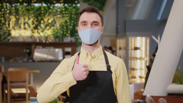 Male Waiter Cafe Owner Wearing Mask and Gloves Stands and Shows Thumb Up