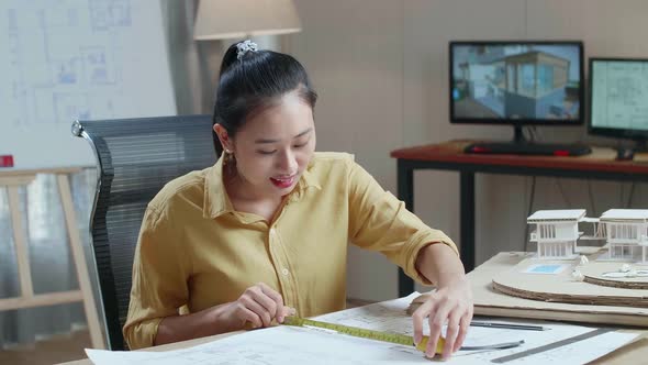 Asian Woman Engineer With A Laptop Measuring Blueprint At The Office