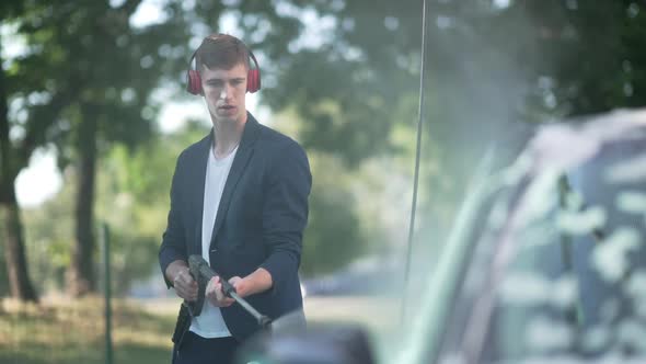 Concentrated Man in Headphones Washing Automobile Outdoors with High Pressure Water Jet in Slow