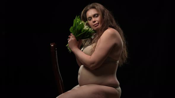 Brunette Caucasian Plus Size Woman with Bouquet of Flowers Sitting on Chair at Black Background