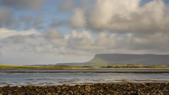 Time Lapse of sea coast of Ireland with hills in the distance and moving clouds in the sky.