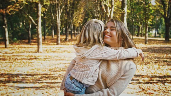 Young Mum Smiling Holding Little Daughter in Arms Hugging and Talking to Her During Their Walk in