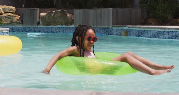 Happy african american girl wearing sunglasses floating on inflatable ring in swimming pool