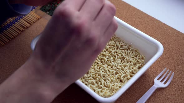 A teenager's hands pour dried vegetables into Chinese noodles. close-up