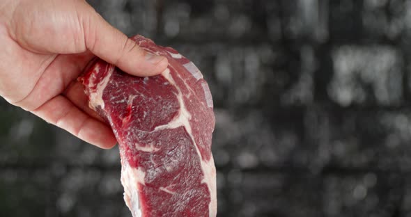 A Man's Hand Holds a Steak Raw Beef Ribeye. 