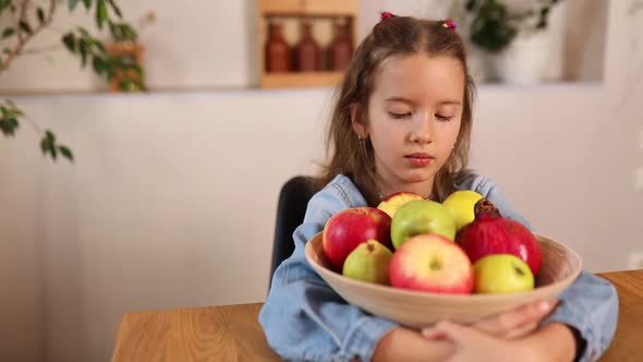 Little happy girl hold bowl with fruits in the kitchen at home, healthy child snack