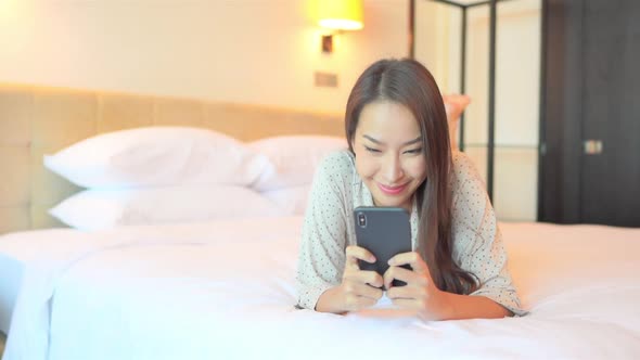 Asian woman texting on mobile phone in bed, a young happy female typing messages on smarthone, full