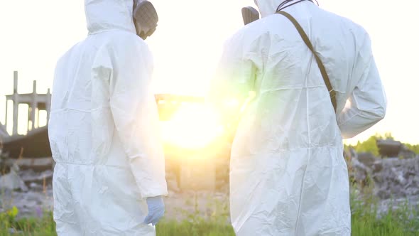 Portrait Two Scientists in Protective Suits and Masks and a Dosimeter Walk Measure Radiation on the