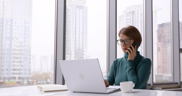 Business woman talking on the phone in the office and working on laptop 