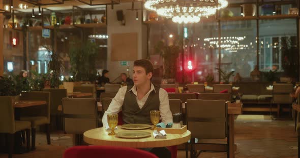 Handsome Young Man Alone Sits in a Stylish Restaurant and Looks Around