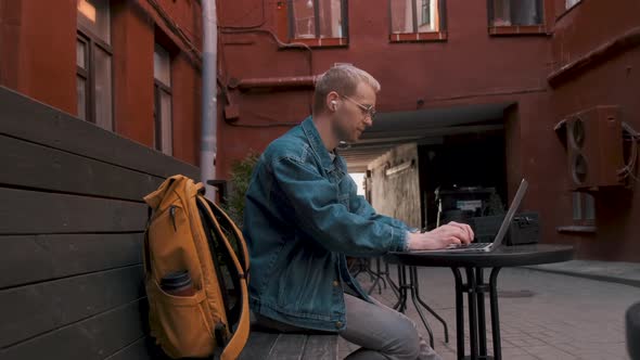 The Traveler Works on a Laptop Sitting at a Table in a Coffee Shop