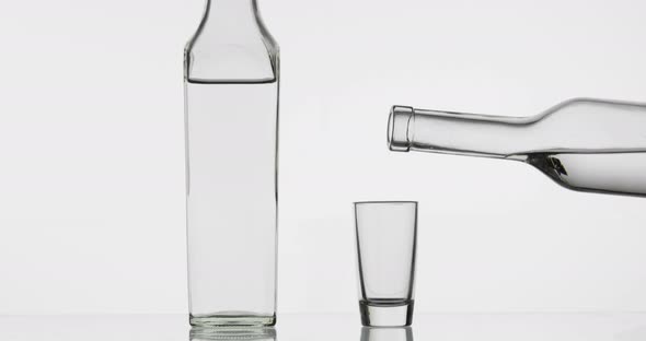 Pouring Up Shot of Vodka From a Bottle Into Glass. White Background