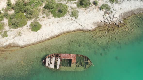 Top shot of a rusted ship wreck laying on a hidden beach. Camera rises up. Close to wide