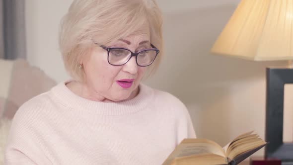 Close-up Portrait of Concentrated Caucasian Old Woman Reading Book, Turning To Camera and Smiling