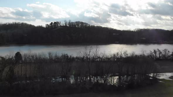 Aerial footage coming down over the park while man is biking and dog is running river in background