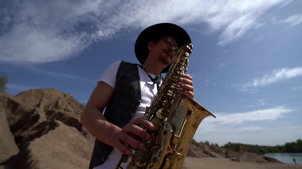 Close-up of a Musician in a Hat Playing Jazz on a Saxophone Standing in the Desert Against a