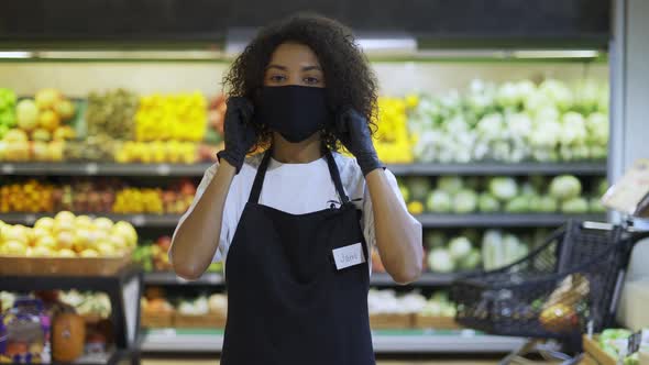 Portrait of Happy African American Female Worker in Black Mask and Gloves Standing in Supermarket