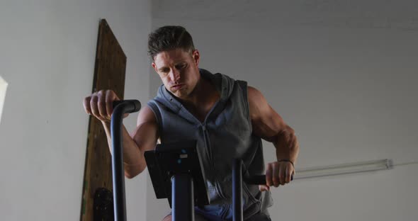 Fit sweaty caucasian man exercising on training bike inside gym