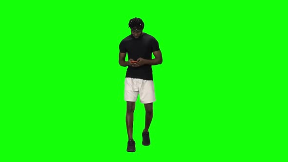 African American Man Is Walking and Texting Message Vie Mobile Phone at Green Screen, Chroma Key