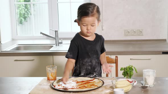 Little Girl Smears a Sheet of Dough with Tomato Paste