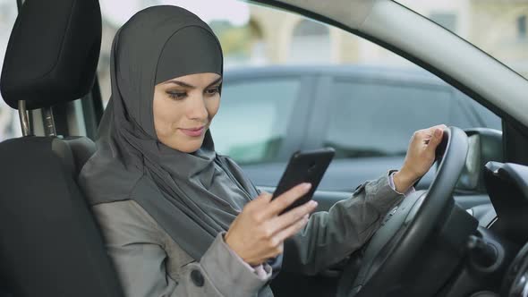 Young Muslim Lady Sitting in Car, Scrolling App on Phone, Searching Best Route