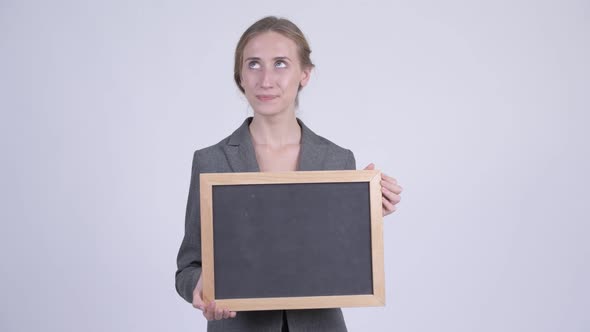 Happy Young Blonde Businesswoman Thinking While Holding Blackboard