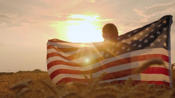 Woman with Usa Flag in the Rays of the Setting Sun Stands in a Wheat Field