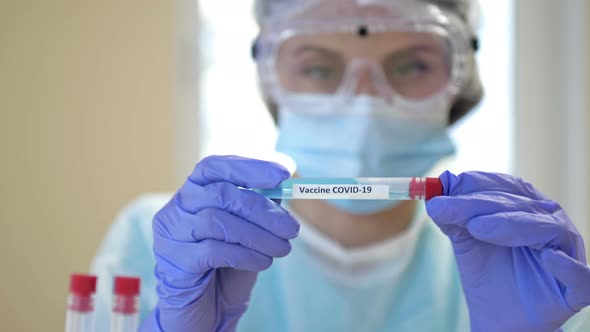 Professional Female Scientist Wearing Glasses and a Mask Holds a 2019Ncov Coronavirus Vaccine Sample